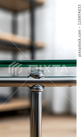 A glass table with a silver frame sits in front of a wooden bookshelf 128954833