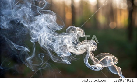 Swirling plumes of white smoke dance against a blurred background of trees, creating an ethereal scene with light and shadow 128954931