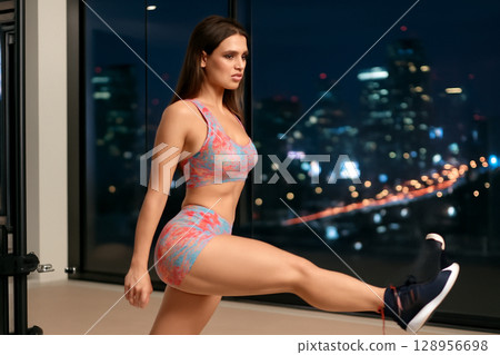 AI generated a fit young woman performs a glute kickback in a sleek gym with a vibrant city backdrop at night. Focus on strength, determination, and modern fitness culture. 128956698