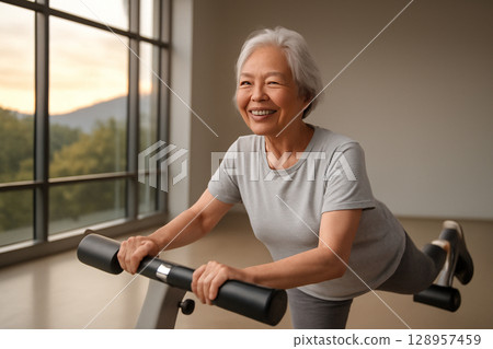 AI generated image of an elderly Asian woman in her 60s smiling and exercising in a spacious gym. She is performing a gentle gluteus minimus exercise with a machine, surrounded by natural light 128957459