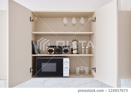 A Modern Kitchen Cupboard that features a Microwave along with elegant Glassware storage 128957673