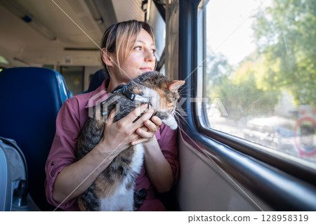 Curious intrigued active cat in woman arms looking through train window during journey, pet travel Curious intrigued active cat in woman arms looking through train window during journey, pet travel 128958319