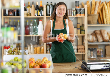 Friendly female salesperson offers to buy ripe apples in produce section of supermarket 128959687