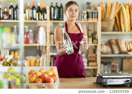 Female salesperson offers to buy a bottle of mineral water in grocery supermarket Female salesperson offers to buy a bottle of mineral water in grocery supermarket 128959709