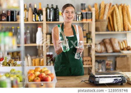 Young woman seller offering water in grocery store Young woman seller offering water in grocery store 128959746