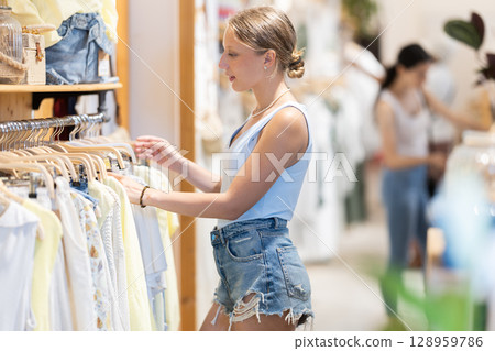 Young girl chooses something in branded clothing store 128959786
