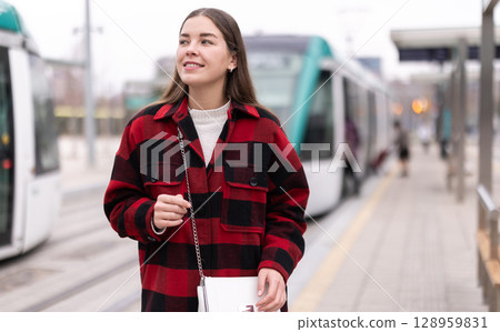 Woman standing at a tram stop 128959831