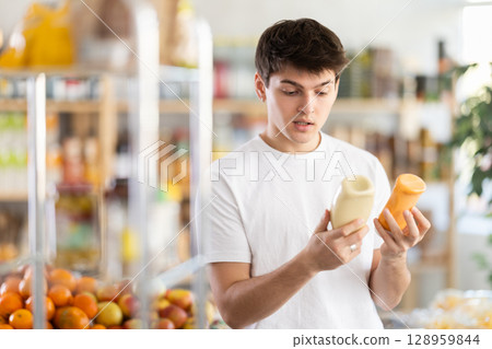 Interested guy choosing natural sauce in grocery store Interested guy choosing natural sauce in grocery store 128959844