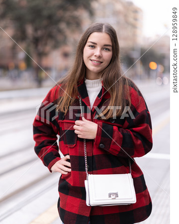 Girl is standing on street platform, waiting for tram to arrive Girl is standing on street platform, waiting for tram to arrive 128959849