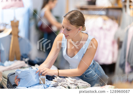 Young woman chooses trousers in clothing store 128960087
