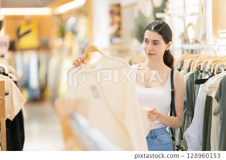 Girl customer chooses blouse in branded store Girl customer chooses blouse in branded store 128960153