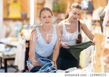 Two girls friends customer chooses denim knee breeches or shorts in store 128960172