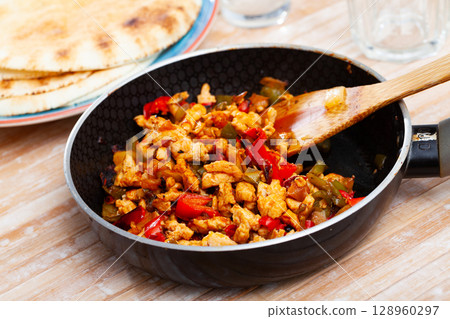 Chicken fajitas with peppers and onion in fry pan with tortillas 128960297