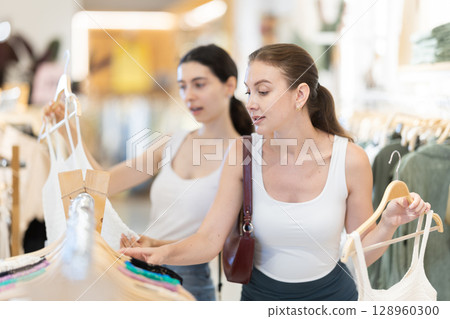 Two girls customer chooses singlet blouse in branded store 128960300
