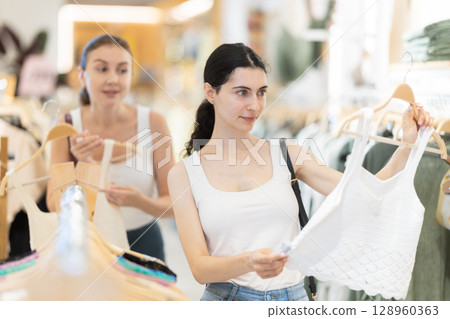 Young woman choosing a tank top on the background of a woman 128960363