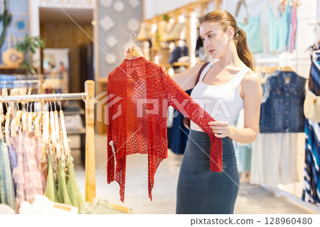 Girl customer chooses knitted jacket in branded store 128960480