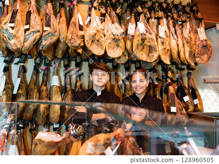 Young couple work together in butcher shop - they cut traditional Spanish jamon 128960505