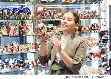Satisfied young woman chooses traditional Spanish souvenirs - miniature mosaic figurine of bull 128960506