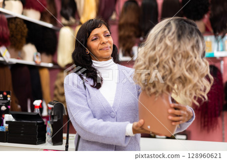 Hispanic woman choosing wigs from natural hair in specialized store Hispanic woman choosing wigs from natural hair in specialized store 128960621