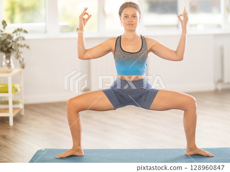 Young woman performing Utkata Konasana with hands in mudra Young woman performing Utkata Konasana with hands in mudra 128960847