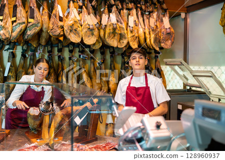 Young man and woman selling spanish jamon at counter 128960937