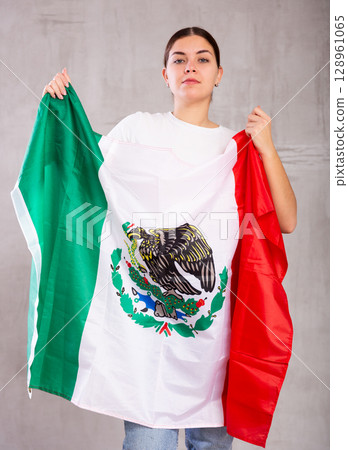 Contented young woman holding Mexico flag against unicoloured background 128961065