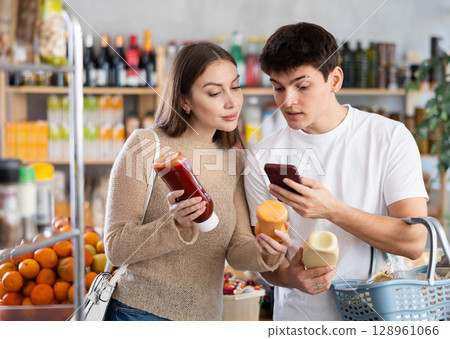 Married young happy couple chooses spicy sauce and scan QR code in supermarket Married young happy couple chooses spicy sauce and scan QR code in supermarket 128961066