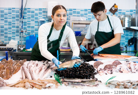 Positive saleswoman demonstrating trout in fish store Positive saleswoman demonstrating trout in fish store 128961082