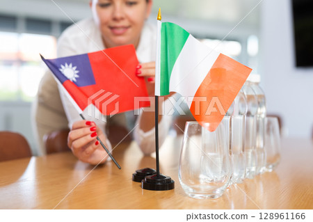 Young woman putting Taiwan and Italy flags on table in office 128961166