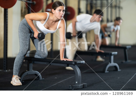 Young woman training with dumbbells on bench Young woman training with dumbbells on bench 128961169