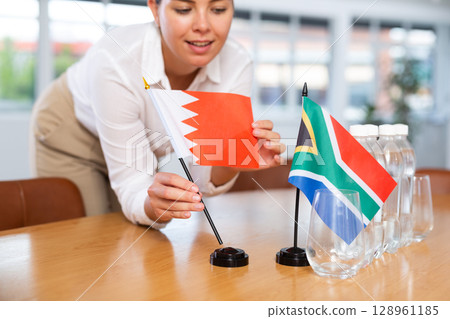 Preparing for business presentation - secretary places flags of Bahraini and South Africa on negotiating table 128961185