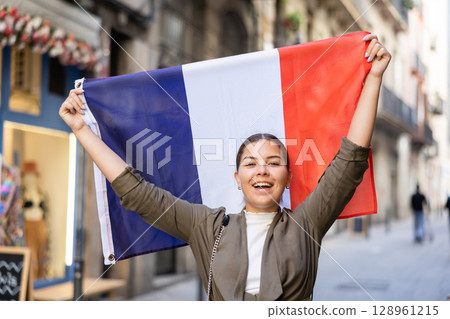 Patriotic young woman waving the flag of France on city street 128961215