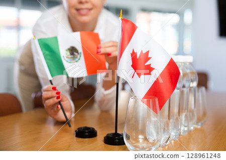 Little flag of Canada on table and flag of Mexico put next to it by young woman Little flag of Canada on table and flag of Mexico put next to it by young woman 128961248