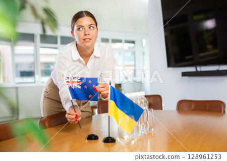 Woman placing flags of New Zealand and Ukraine on negotiating table 128961253
