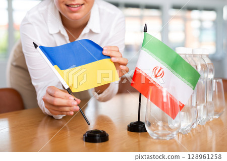 Preparing for business presentation - secretary places flags of Ukrain and Iran on negotiating table 128961258