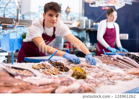 Positive salesman demonstrating calamary in fish store 128961262
