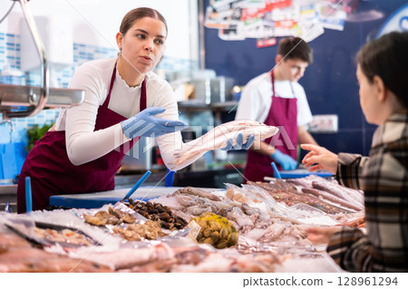 Smiling saleswoman demonstrating red snapper to purchaser in fish store 128961294