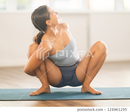 Sportive girl practicing frog pose of yoga in light room 128961295