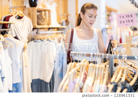 Young woman choosing blouse and trousers in clothing store 128961331
