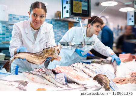 Positive saleswoman holding cod fish in fish store Positive saleswoman holding cod fish in fish store 128961376
