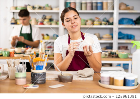 Young woman painting pottery in workshop 128961381