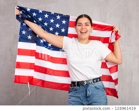 Happy girl stands with flag of USA. Isolated on gray background Happy girl stands with flag of USA. Isolated on gray background 128961419