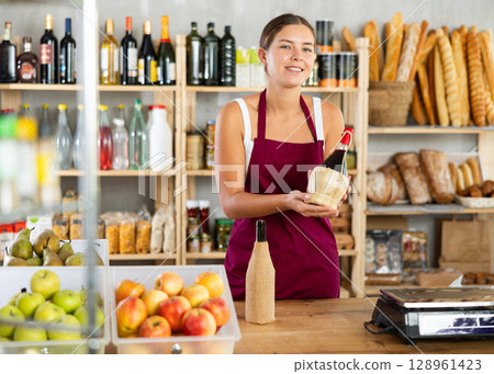 Young female seller offering wine in grocery store 128961423