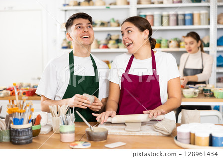Joyous young man and woman sculpting handmade cups 128961434