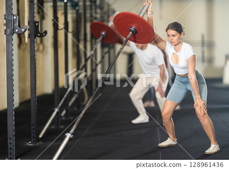 Young woman training with barbell with one arm Young woman training with barbell with one arm 128961436
