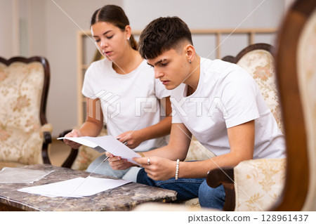 Young couple is studying the documents and signing them Young couple is studying the documents and signing them 128961437