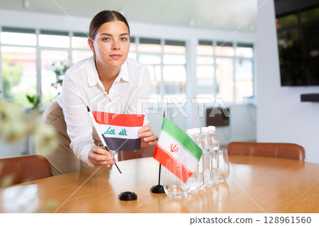 Positive young woman putting little flag of Iraq on table next to the flag of Iran Positive young woman putting little flag of Iraq on table next to the flag of Iran 128961560