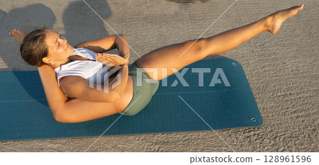 On windy day young slender woman does yoga near sea doing yoganidrasan On windy day young slender woman does yoga near sea doing yoganidrasan 128961596