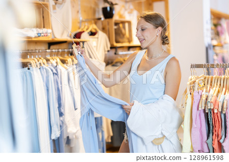 Girl customer chooses trousers in branded store Girl customer chooses trousers in branded store 128961598
