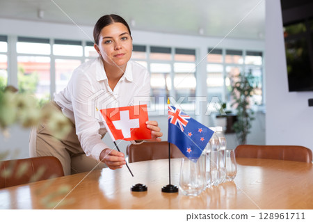 Young woman puts flags of Switzerland and New Zealand on table in office 128961711